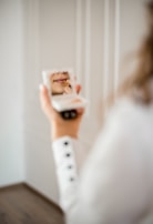 A smiling woman applying lipstick in front of a mirror with soft lighting.