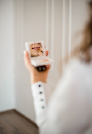 Close-up of a hand applying lipstick in a softly lit room.