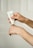 A person's hands are applying cream from a tube labeled 'G&H' onto the back of one hand. The background is soft and neutral, creating a minimalistic look.