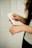 A person is applying a cream or lotion from a tube labeled G&H onto their hand. The focus is on the hands and the tube, with a neutral, soft background. The person has long, curly hair visible in the corner.