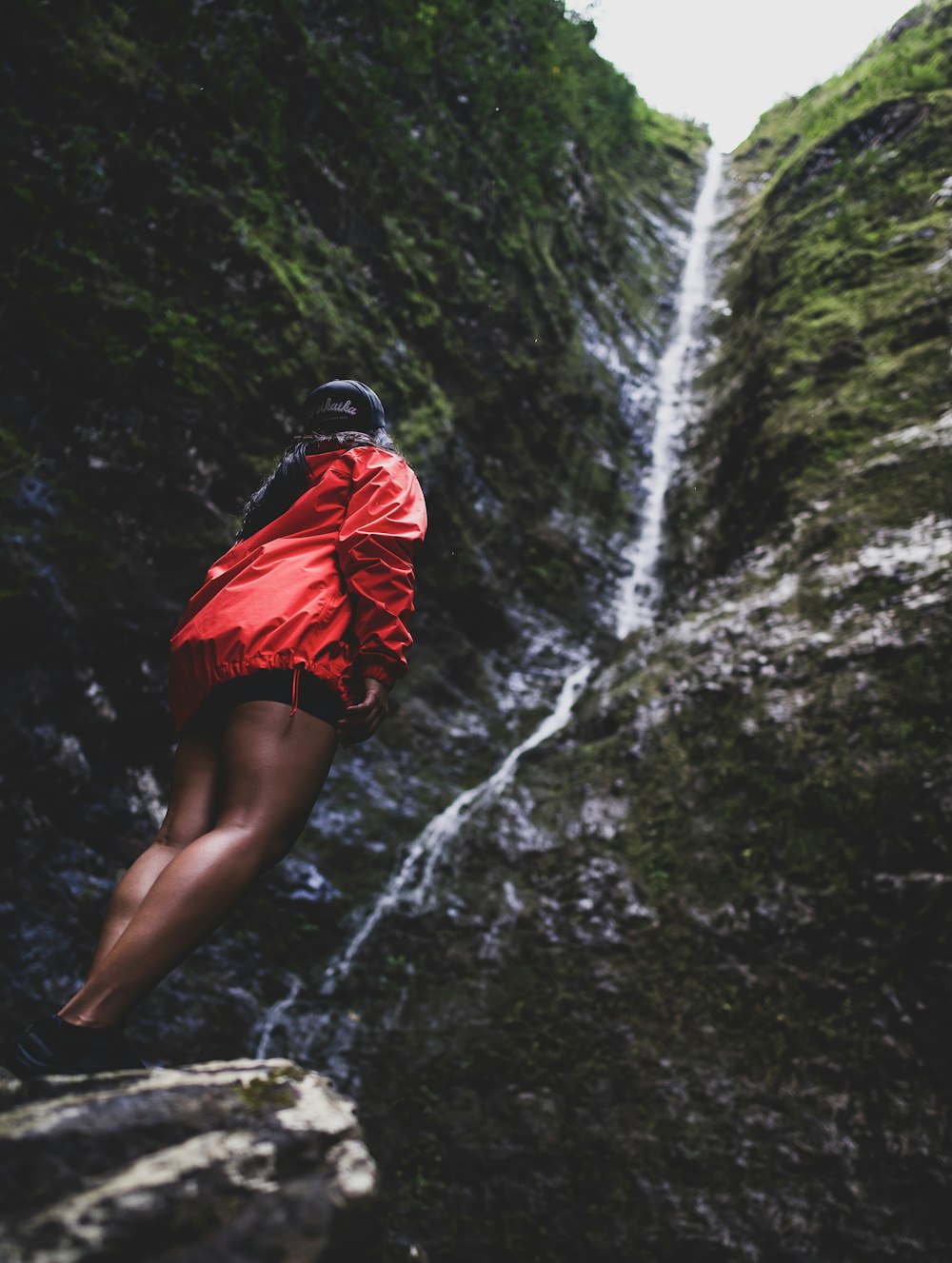 woman in red and black dress standing on rock near waterfalls during daytime