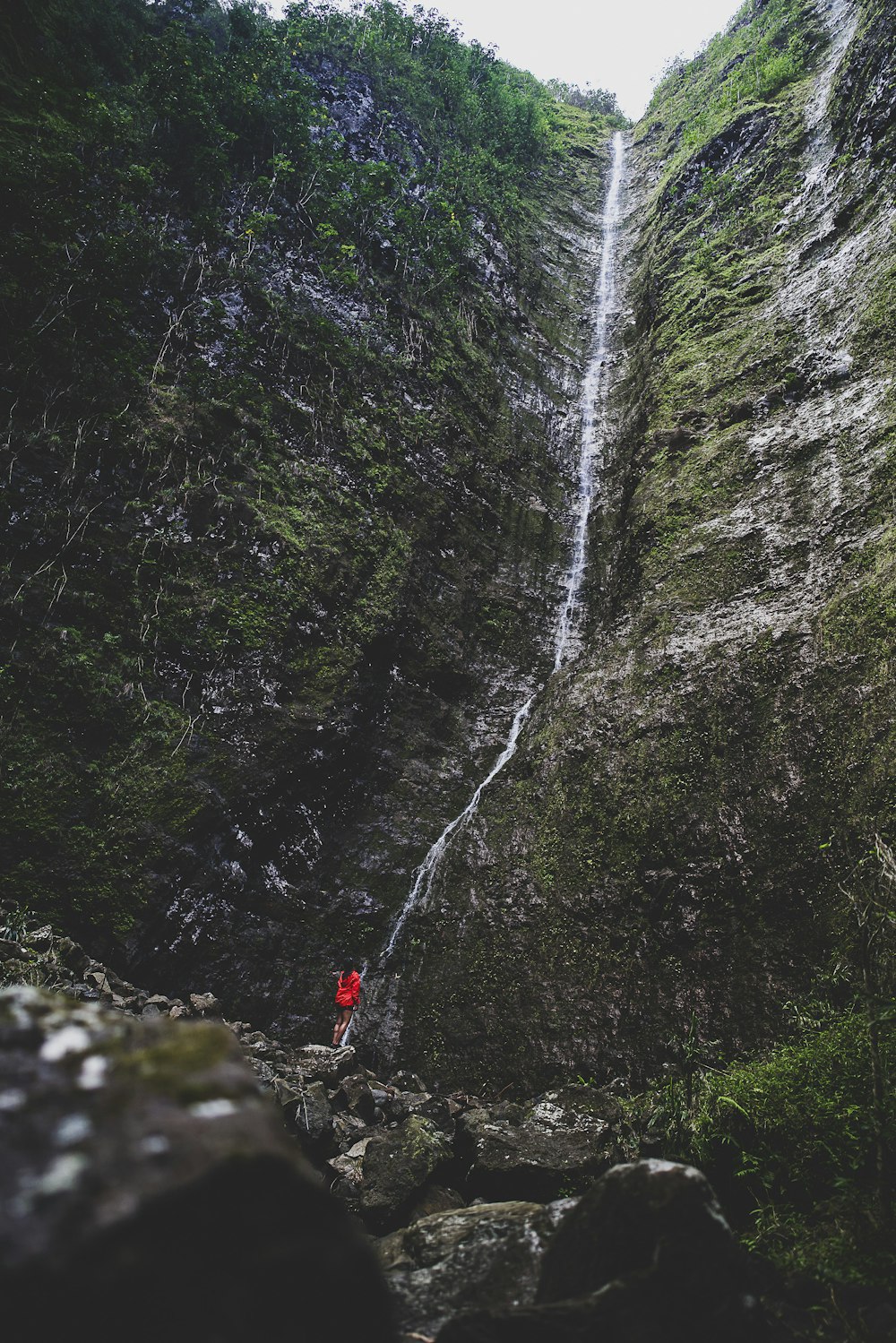 person in red jacket standing on rock near waterfalls during daytime