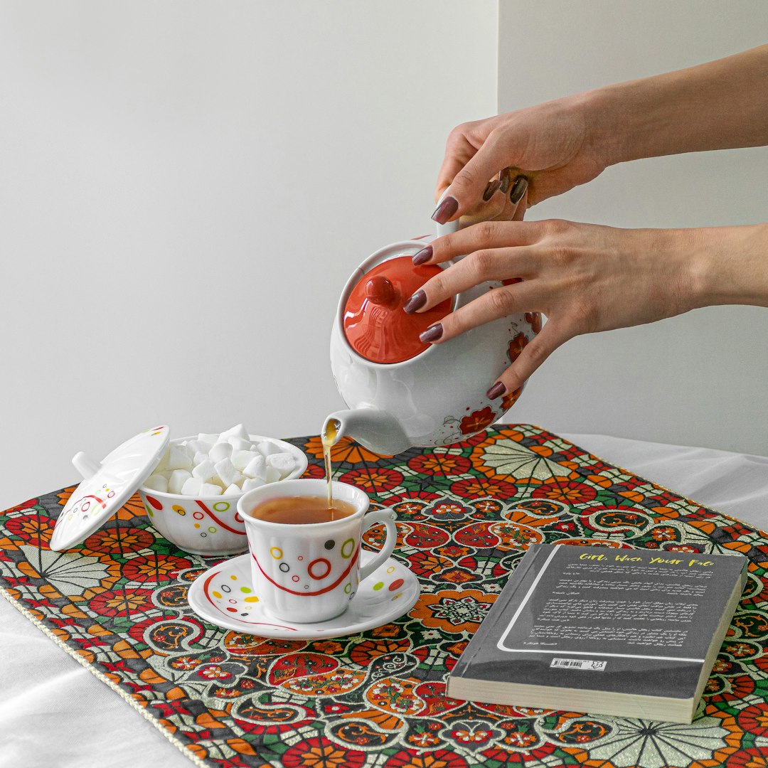 person holding red ceramic mug on white and red floral ceramic saucer