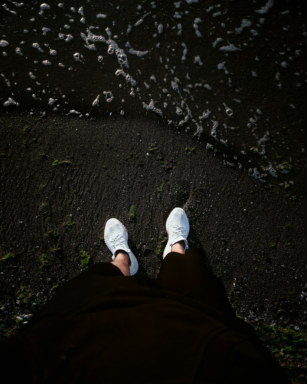 Persona con pantalones negros y zapatillas blancas de pie en un terreno rocoso