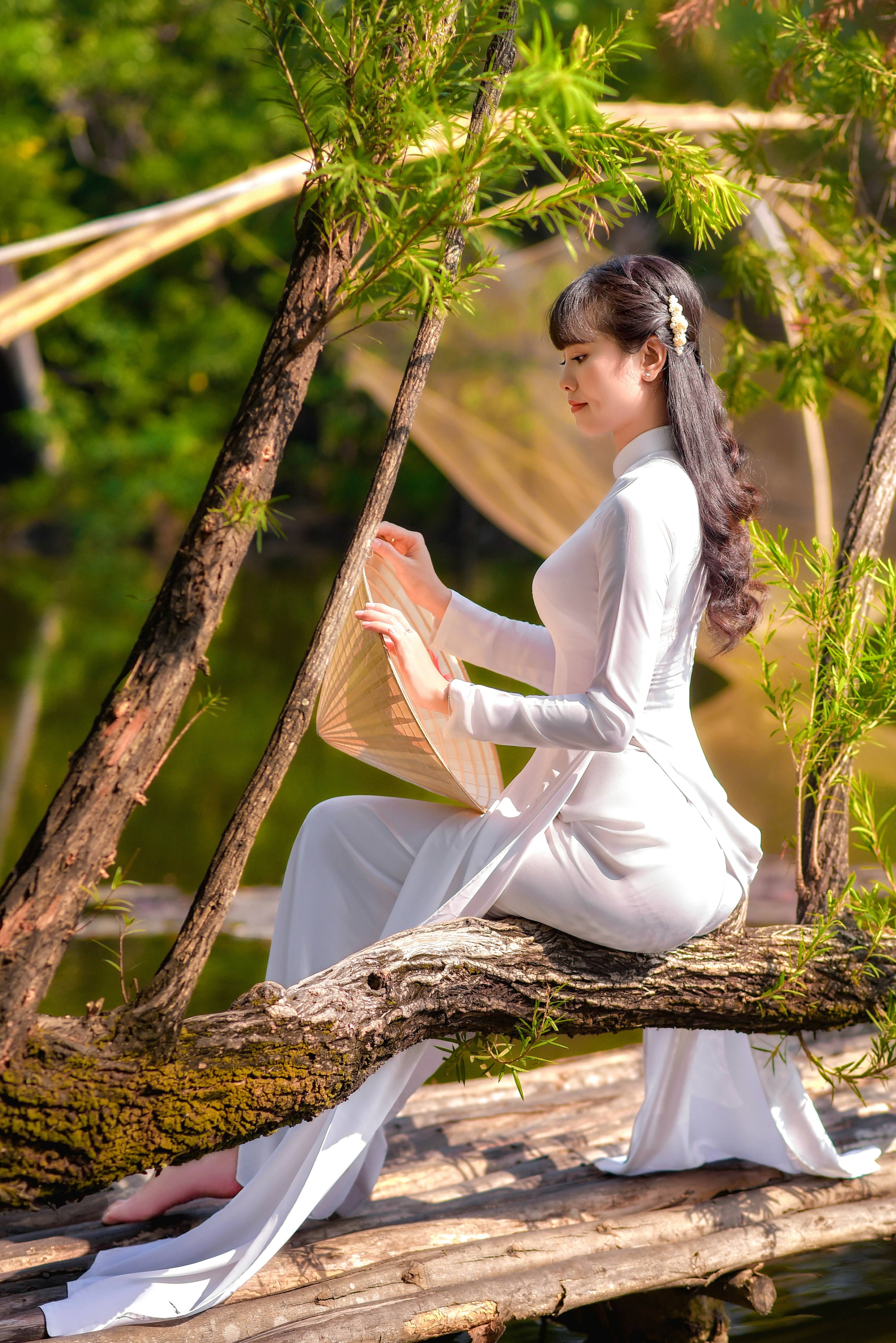 woman in white long sleeve dress sitting on brown tree branch during daytime