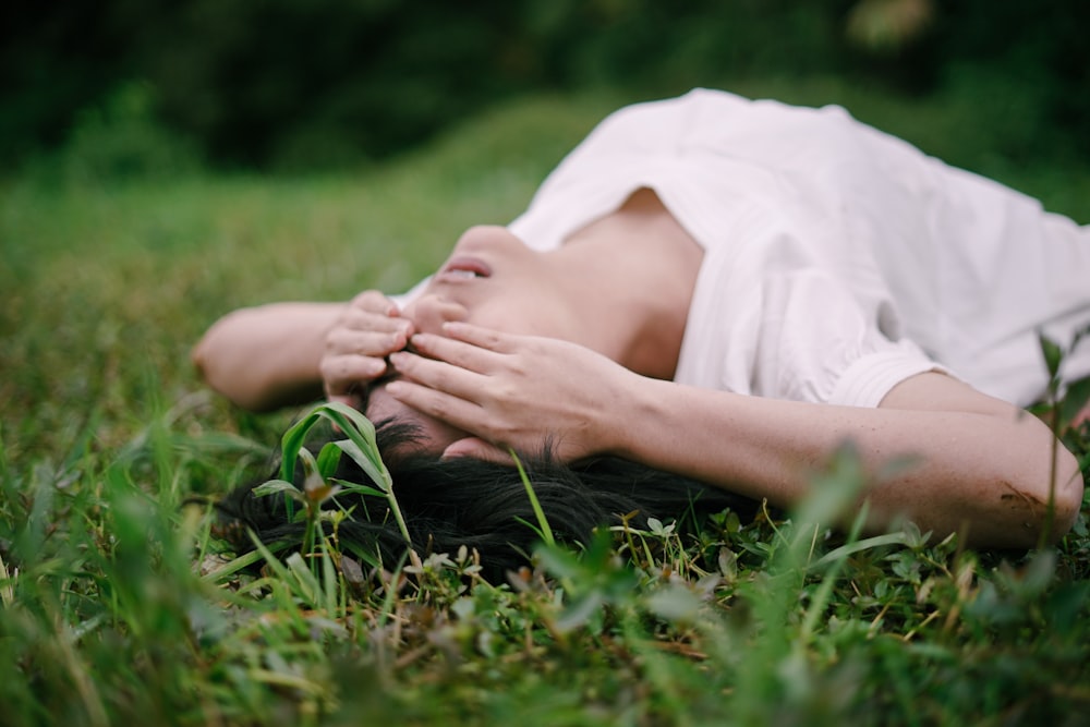 woman in white dress lying on green grass during daytime