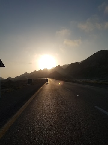 A rugged motorcyclist riding along a winding mountain road at sunset.