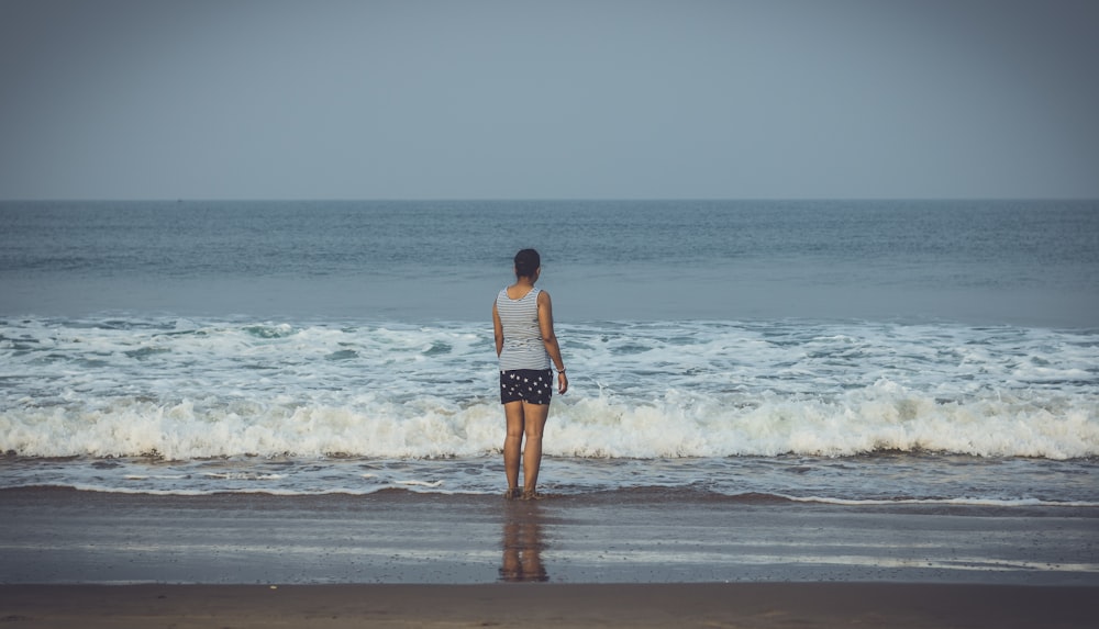 woman in white and black stripe tank top and black shorts standing on beach during daytime