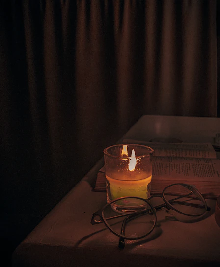 A cozy scene with a white candle lit on a wooden table beside an open Bible and a small green plant.