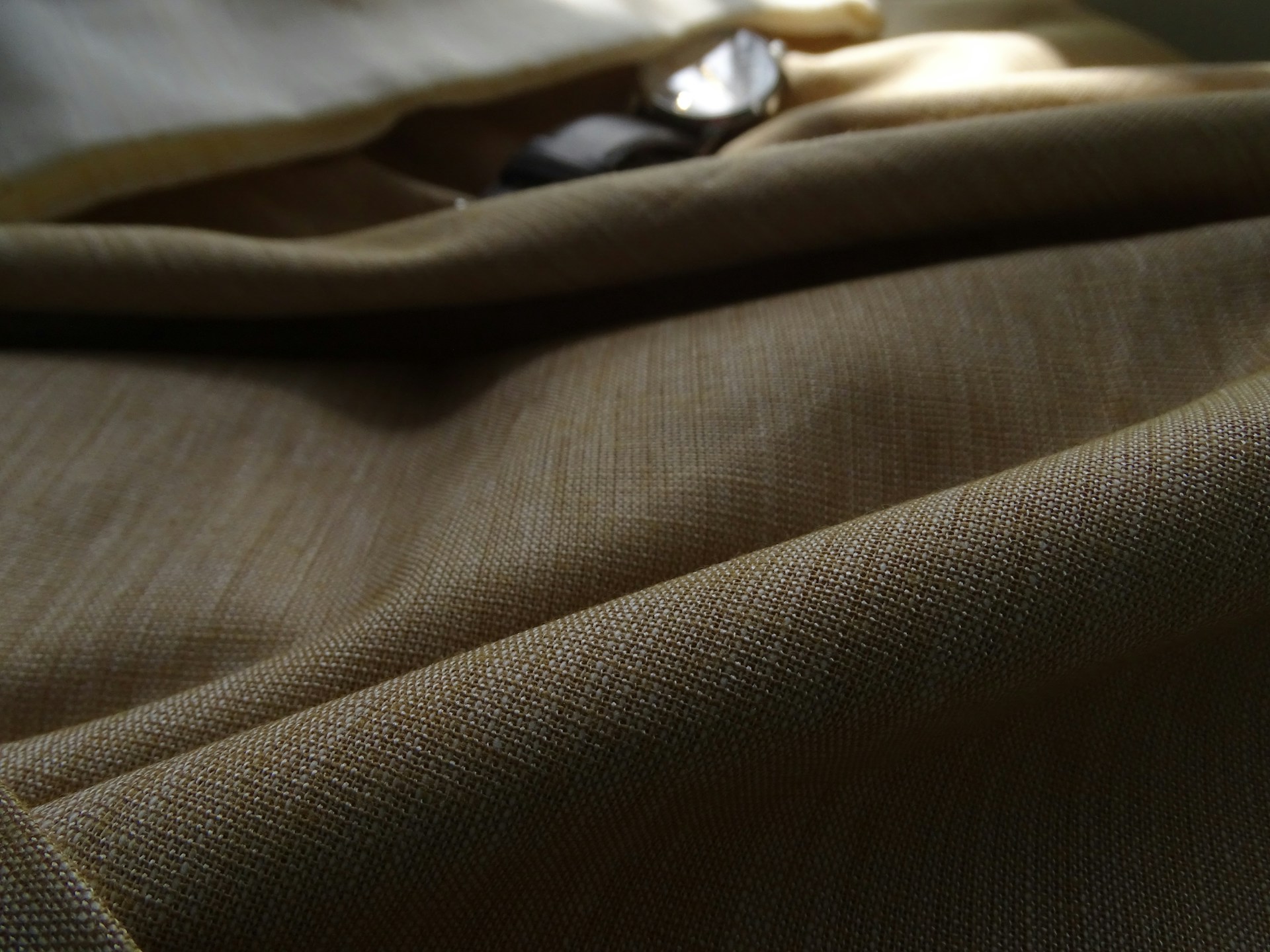 Close-up of luxurious fabric texture in warm beige tones, highlighting the fine weave and subtle sheen of the cover-up.