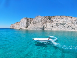 white and blue boat on blue sea near gray rocky mountain during daytime