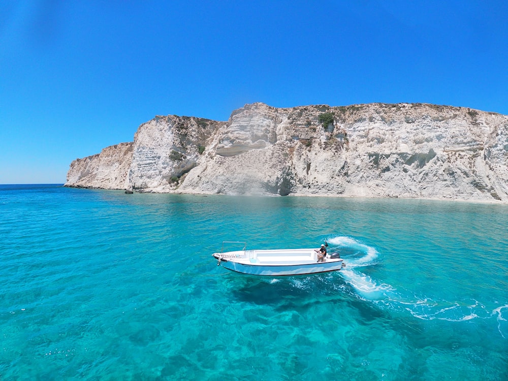 white and blue boat on sea near gray rocky mountain during daytime