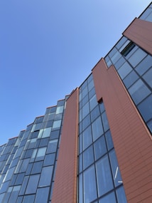The image features a modern building facade with large glass windows and sleek brown panels against a clear blue sky.