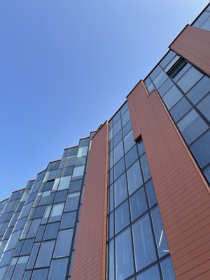 The image features a modern building facade with large glass windows and sleek brown panels against a clear blue sky.