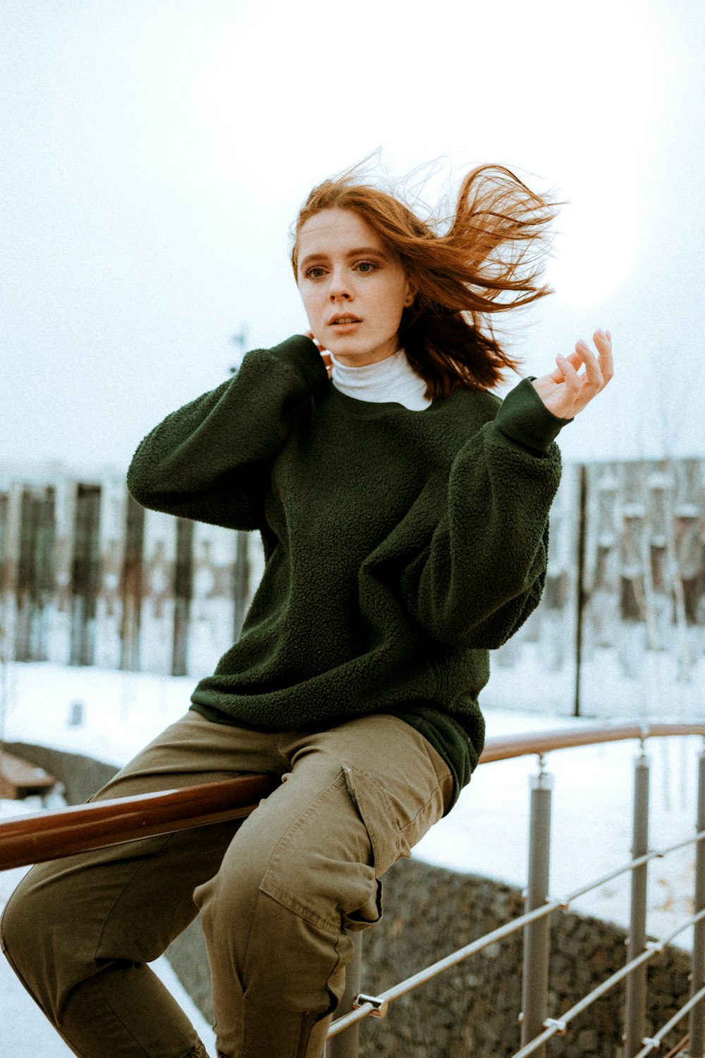 Femme en pull vert assise sur un banc en bois brun pendant la journée