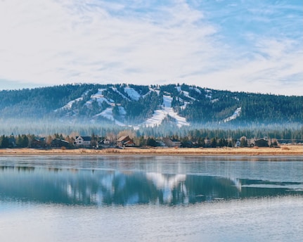 snow covered mountain near lake under cloudy sky during daytime