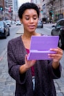 woman in gray cardigan holding pink tablet computer