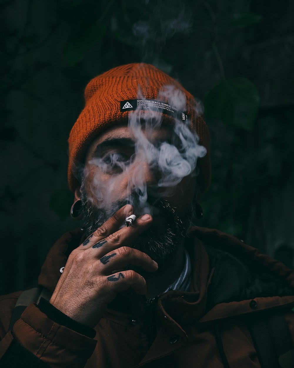 man smoking cigarette wearing orange knit cap and black jacket
