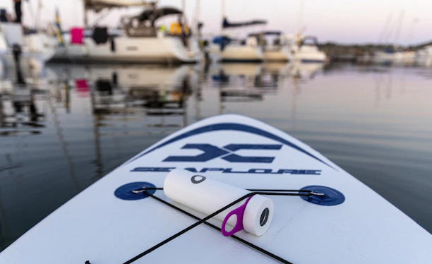 A vibrant stand-up paddle board resting on calm, crystal-clear lake water at dawn.