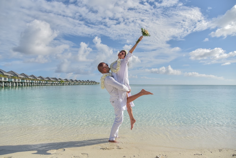 man in white dress shirt and white pants standing on beach during daytime