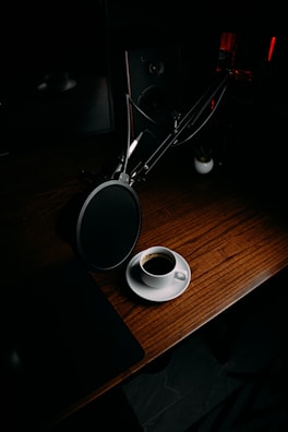 A close-up of a coffee cup with a podcast microphone in the background.