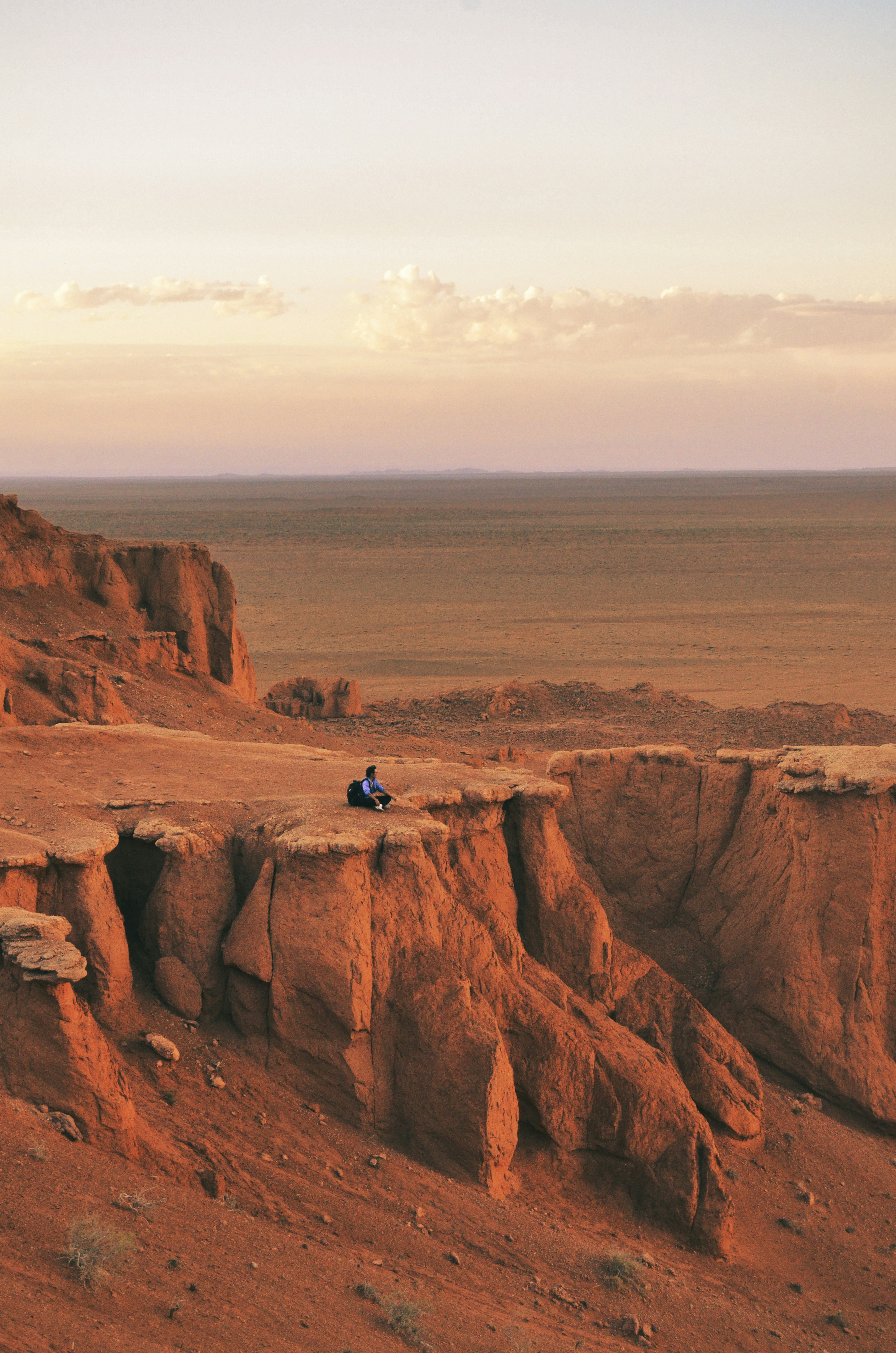 Man in blue jacket sitting on brown rock formation during daytime