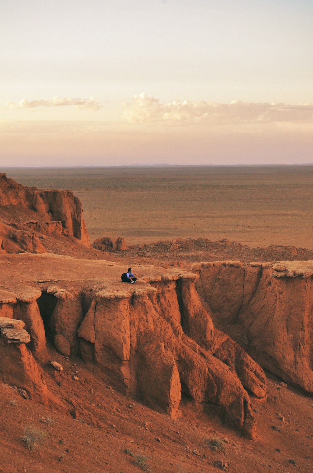 man in blue jacket sitting on brown rock formation during daytime
