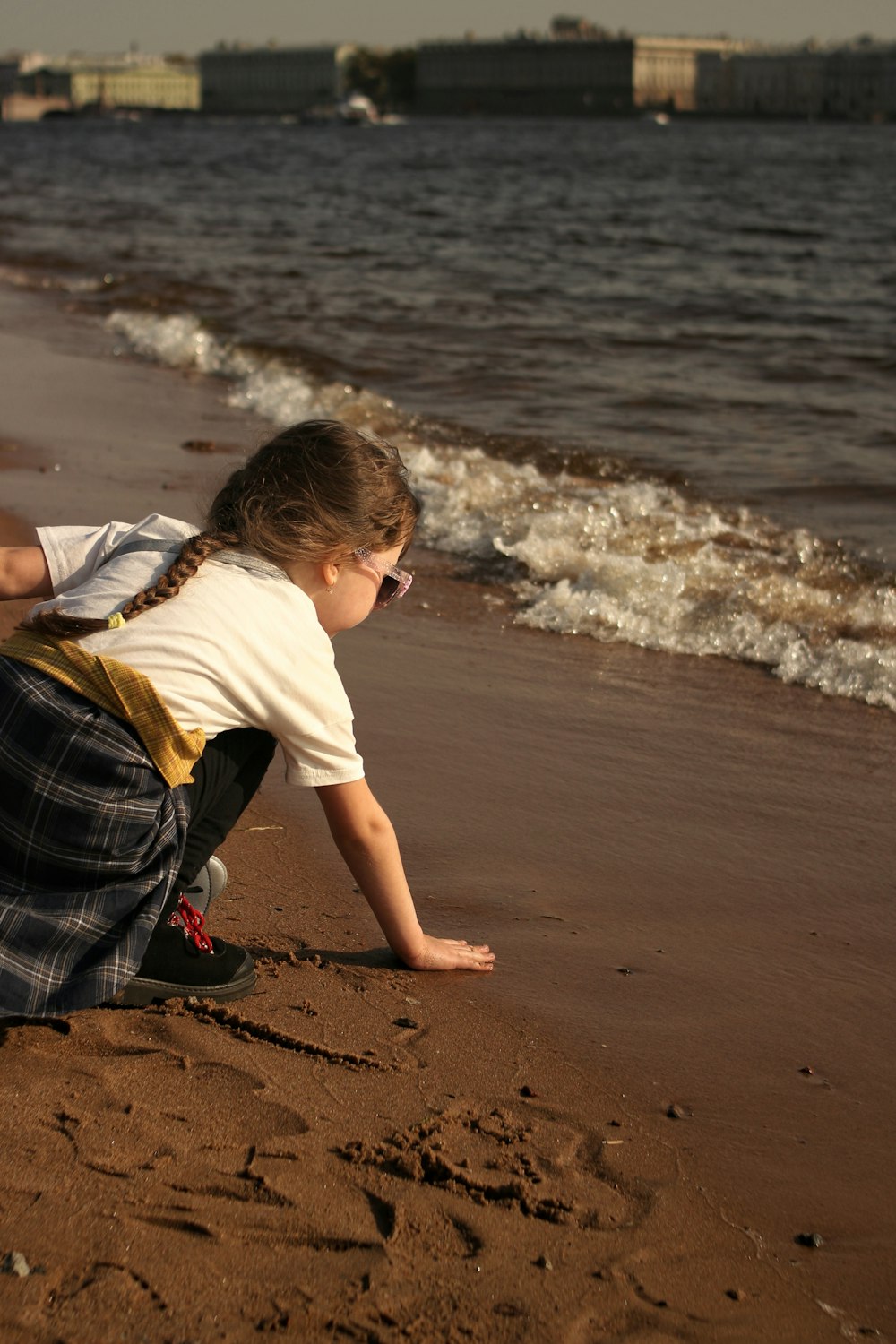 boy in white t-shirt and blue and white plaid shorts sitting on beach shore during