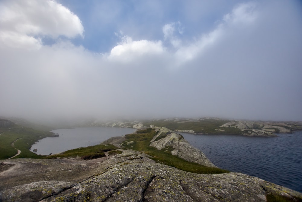 green grass covered hill by the sea under white clouds and blue sky during daytime