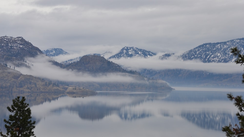 body of water near mountain under white clouds during daytime