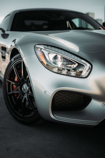 A sleek silver sports car is prominently shown, highlighting its rounded headlight and front tire. The design is modern and aerodynamic, with sharp lines and a luxurious appearance.