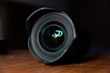 A close-up of a camera lens on a wooden table.