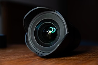 A close-up of a camera lens resting on a wooden table outdoors.