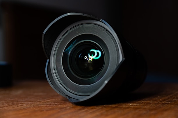 Close-up of a high-quality camera lens reflecting natural light on a wooden table.
