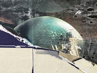 A collage-like composition featuring layers of torn paper, revealing textures and images beneath. The central focus is a circular, globe-like object with a greenish hue and reflective surface, partially covered by other materials. The background consists of dark, weathered textures with scattered lighter spots resembling a night sky.