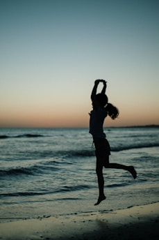 woman in white shirt and black pants standing on beach during sunset
