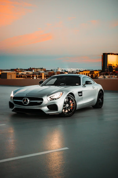 A sleek European sports car parked in front of an urban skyline at sunset.