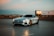 A sleek luxury car parked beside a modern city skyline at dusk.