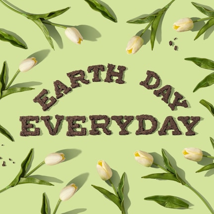 The image features the words 'EARTH DAY EVERYDAY' made from soil or mulch, placed centrally against a pastel green background. Surrounding the text are white tulips with long green leaves, radiating outwards in a pattern.
