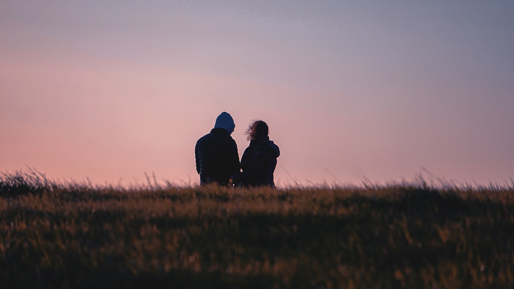 a couple of people sitting on top of a grass covered field