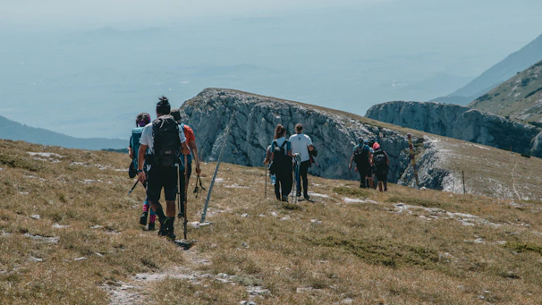 A group of travelers with backpacks and trekking poles exploring a scenic mountain trail.