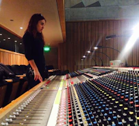 A producer working intently at a mixing console surrounded by gear.