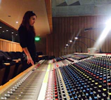A young girl smiling brightly as she adjusts sound levels on a mixing board.