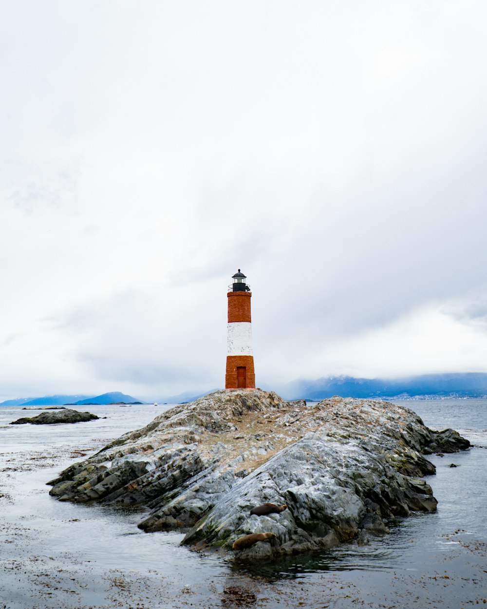 Faro marrone e bianco sulla formazione rocciosa grigia vicino allo specchio d'acqua durante il giorno