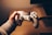 A person is holding a white gaming controller with both analog sticks and various buttons visible. The setting appears cozy, with warm lighting creating a relaxed atmosphere. The background includes a wooden surface, possibly a desk or table.