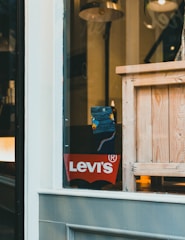 A store display with a Levitating Levi's logo on a red background is visible through a window. Inside, there is a wooden crate and a floor lamp with a metallic shade. A patterned sock or piece of fabric is partially visible near the center.