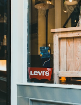 A store display with a Levitating Levi's logo on a red background is visible through a window. Inside, there is a wooden crate and a floor lamp with a metallic shade. A patterned sock or piece of fabric is partially visible near the center.