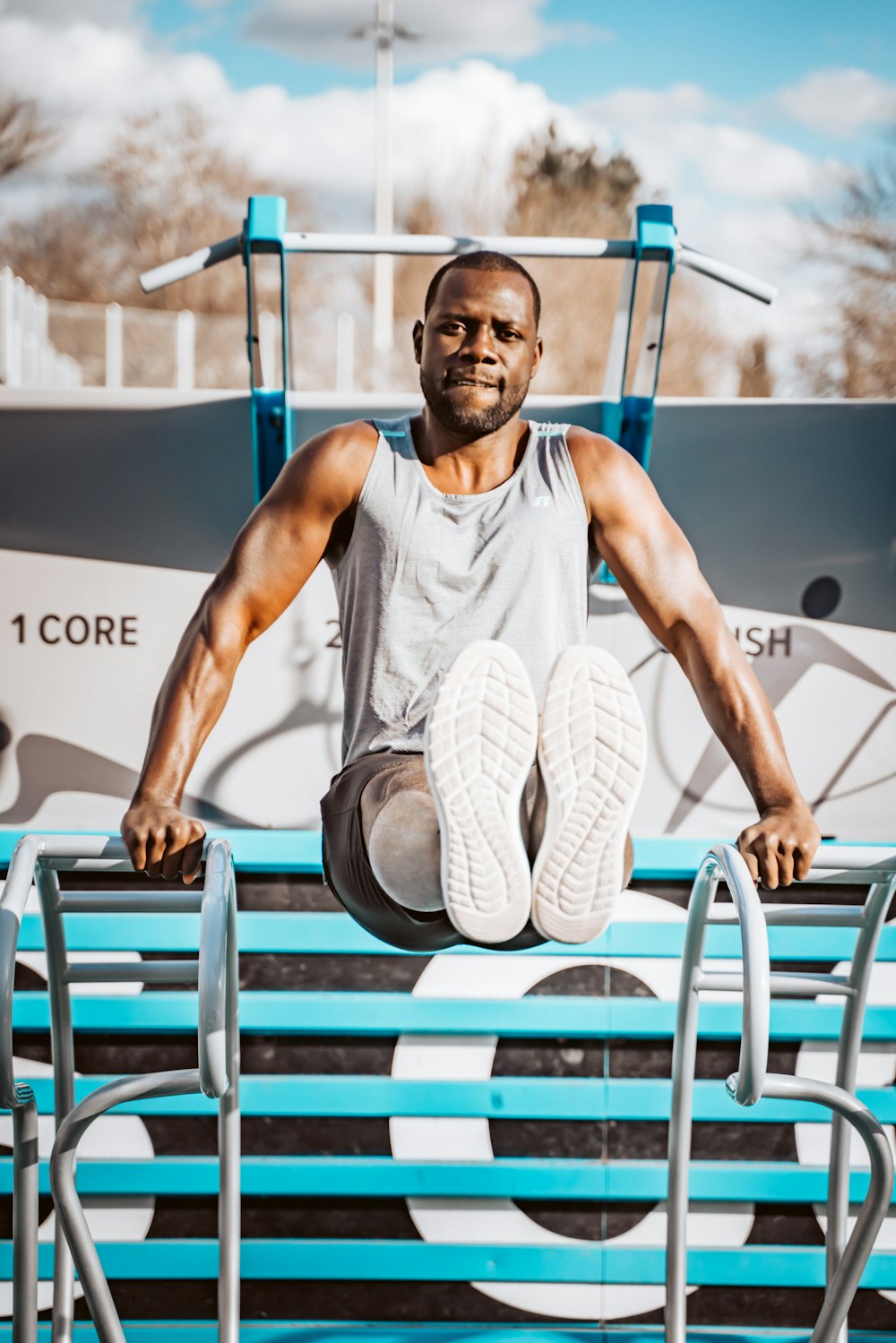 man in white tank top sitting on blue wooden bench during daytime