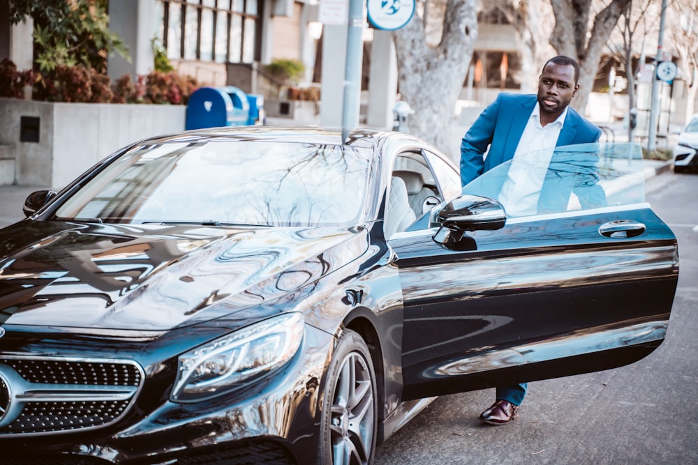 man in blue suit standing beside black car