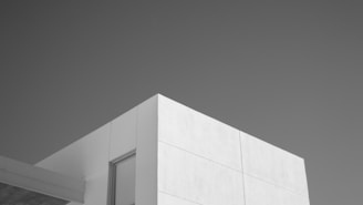 A minimalist photograph of a modern building corner, prominently featuring smooth white walls and clean geometric lines against a clear sky.